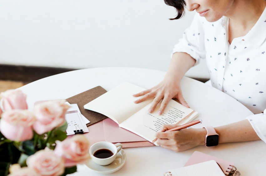 femme qui ecrit dans un carnet avec un cafe et des fleurs