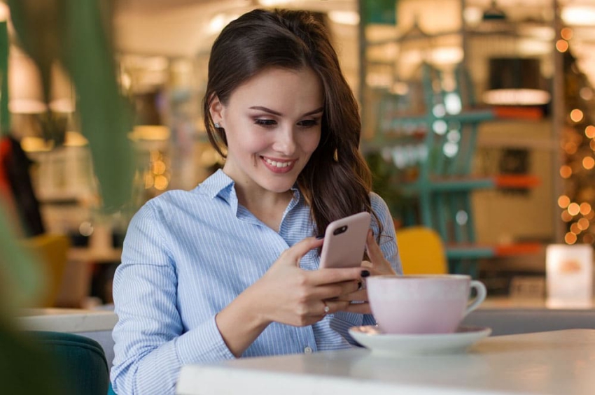 jeune femme assise a un terrasse avec un cafe sur son telephone