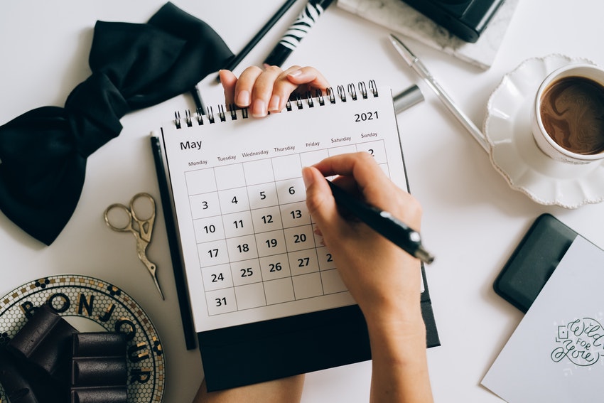 femme qui ecrit dans un calendrier ouvert au mois de mai avec un cafe et un stylo