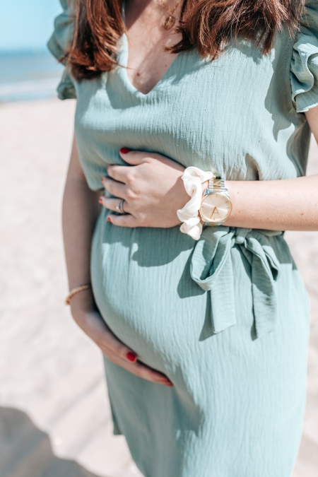 femme enceinte qui tient son ventre en robe verte sur la plage